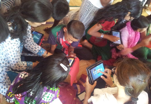 Children exploring tablet with the help of CREATE team members
